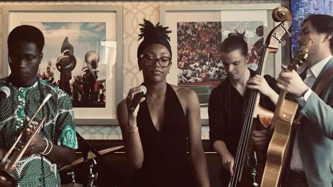 Four people make music -- three hold instruments and one holds a microphone