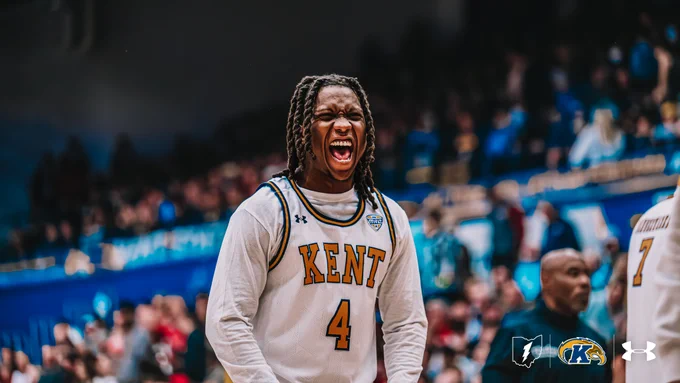 Kent State men's basketball player Jamal Sumlin, wearing number 4 in a white Kent home jersey, roars with intensity on the court during a game against Miami. A blurred crowd fills the background.