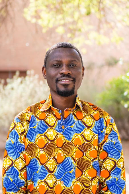 Eric Aglozo wearing a colorful patterned shirt outdoors with trees and a building in the background.