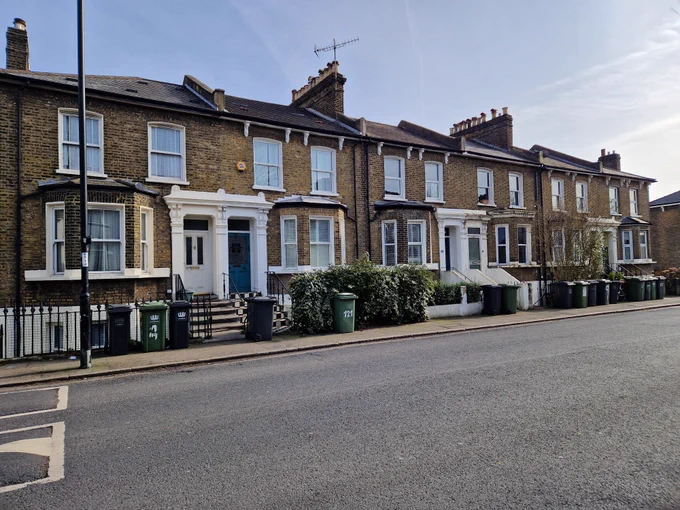 Row of traditional two-story brick terraced houses with white-framed windows and front steps on a quiet street.