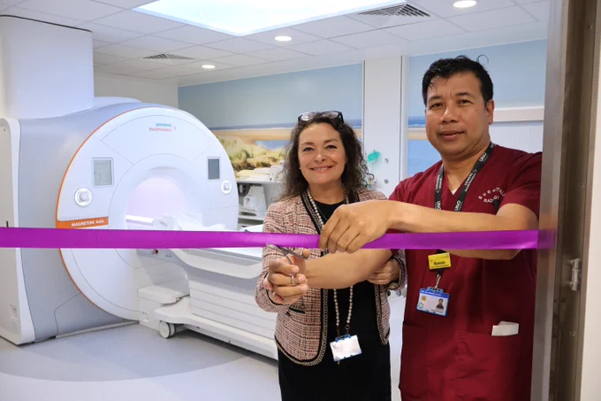 Deputy Chief Executive Fiona Wheeler stands alongside a staff member in maroon scrubs as she smiles and cuts a purple ribbon to officially open the new MRI scanning suite.