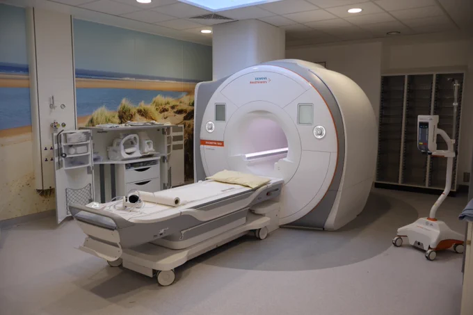 A brand new, large white MRI scanner machine inside a brightly lit, clean hospital room.
