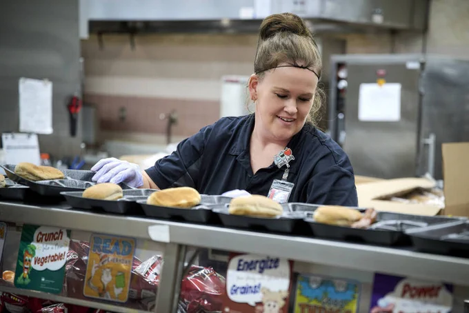 Photo of woman in hairnet preparing meals in a cafeteria kitchen
