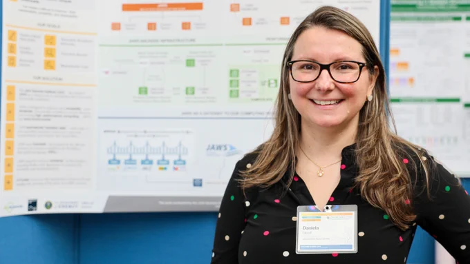 Daniela Cassol of Lawrence Berkeley National Laboratory stands in front of her research poster and smiles for a portrait during the 2026 Oak Ridge Leadership Computing Facility User Summit poster session.