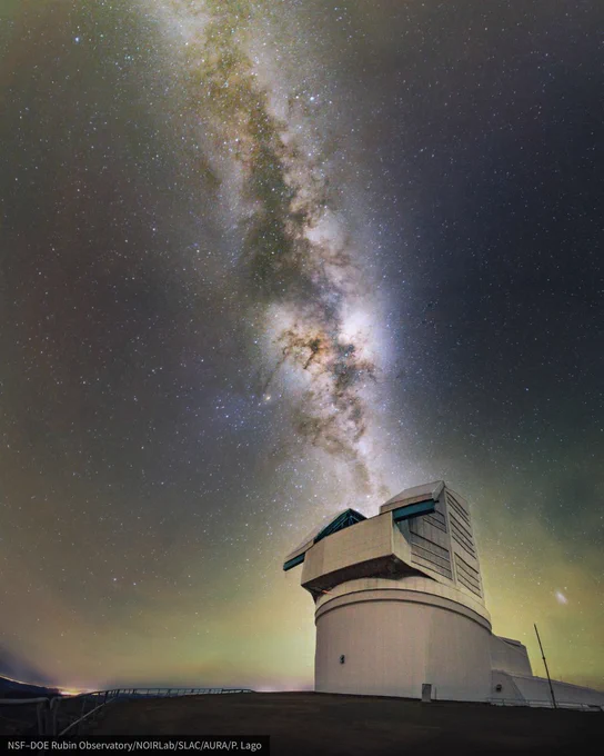 Vertical panorama of a large white observatory under a starry sky. The Milky Way stretches diagonally overhead with faint green airglow near the horizon.