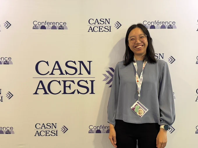 PhD candidate Joey Wong standing and smiling in front of a CASN/ACESI conference backdrop.