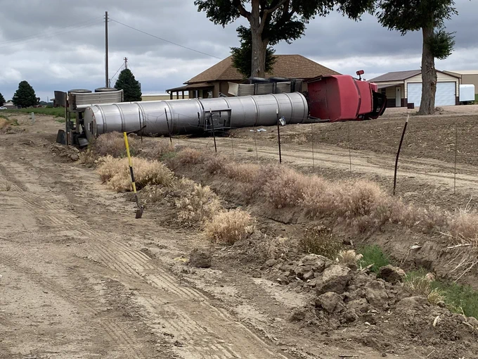Image of a semi on its side in a field near a house.