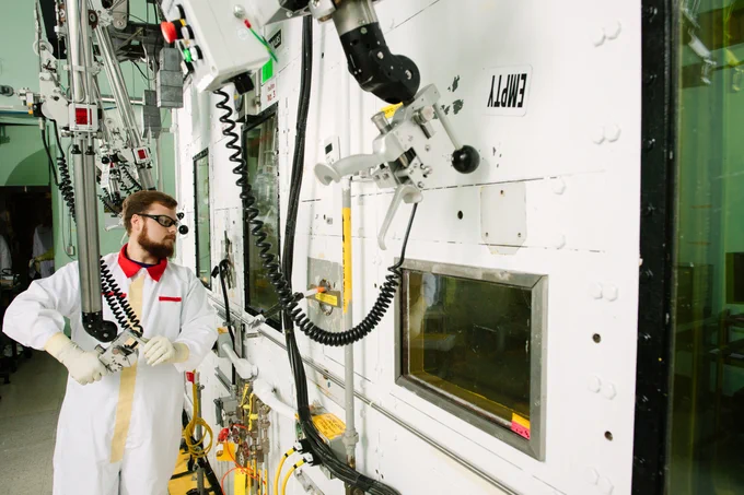 From behind shielded glass, scientist Caleb Mortensen guides a mechanical manipulator, reflecting the lab’s commitment to safer, faster work.
