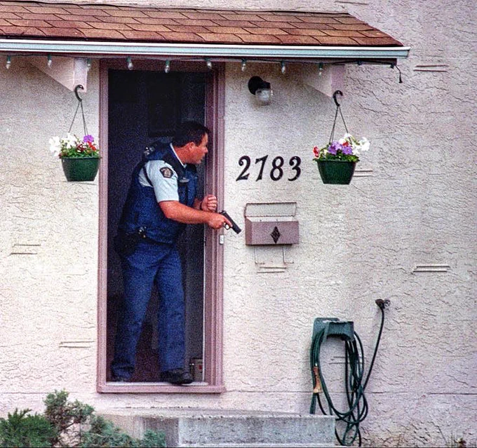 A RCMP officer cautiously looks for a suspect at a residence in Kelowna, British Columbia, Canada in 1996. Gary Moore photo. Real World Photographs. #photojournalism #Canada #Grok #Nikon #crime #realworldphotographs #photography #RCMP  #garymoorephotography #Kelowna #BC