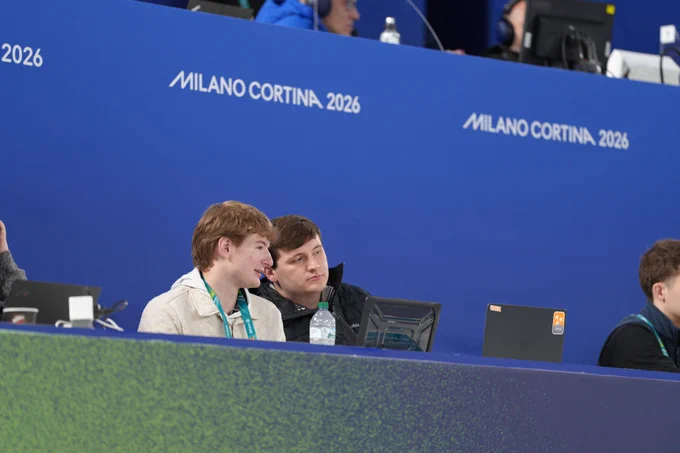 Two people sitting at a desk with laptops against a "MILANO CORTINA 2026" blue backdrop.
