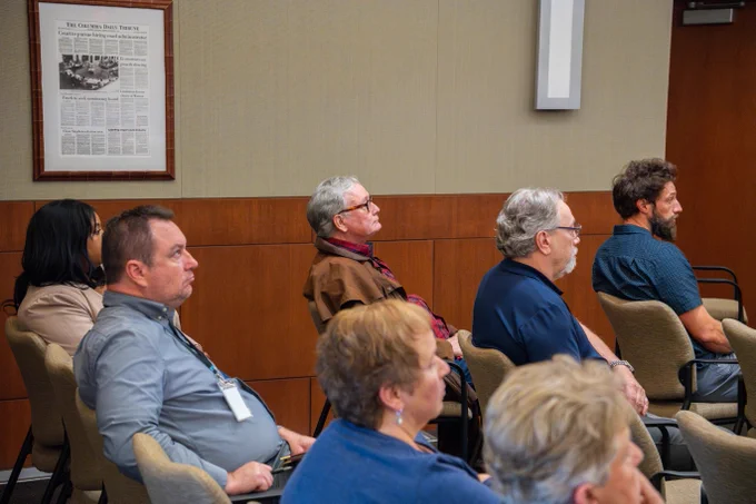 A group of adults seated in a conference room attentively listening to a presentation or speaker.