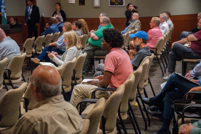 Audience seated in rows inside a conference room, attentively listening to a speaker out of frame.