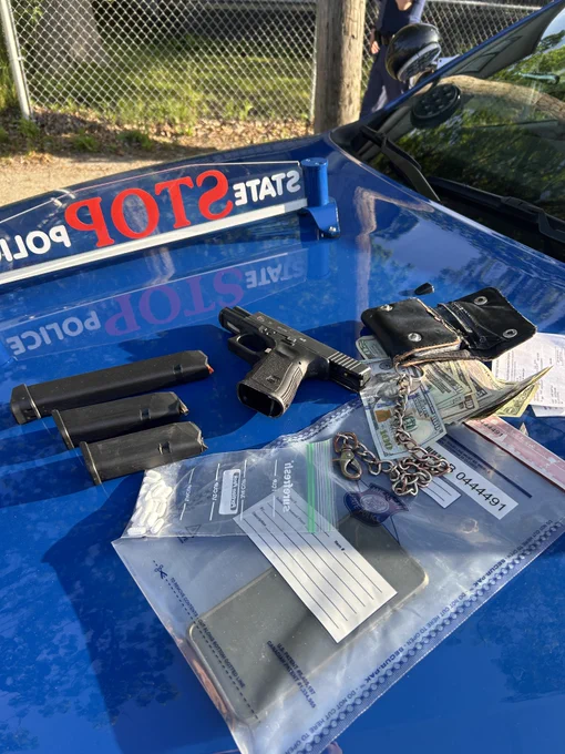 Photograph of handgun, ammunition magazines, and currency that were seized during a traffic stop. The picture is taken on the hood of a Michigan State Police patrol vehicle.