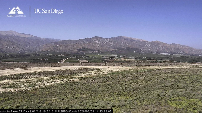 A dry scrubby valley landscape with agricultural fields at the foot of distant mountains. The sky is blue with no clouds. ALERTCalifornia and UC San Diego's logos are in the upper left corner. 