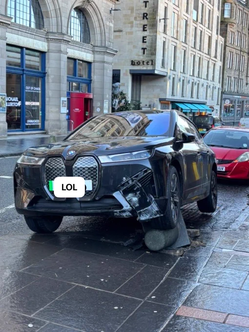 A black electric BMW sits on top of a bollard. A truly loving relationship.