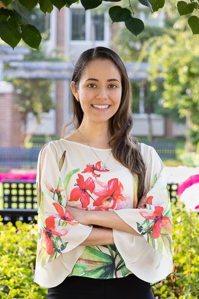 Soledad Soverina smiles at the camera. She is standing in a garden. 