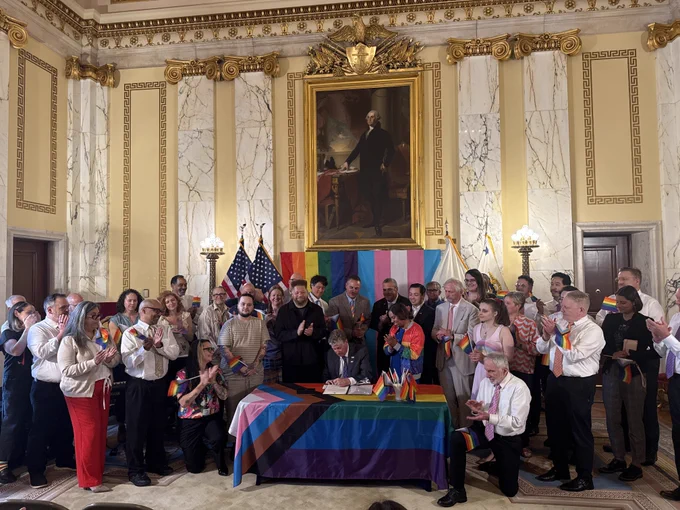 Photo of people crowding around the governor signing a proclamation in the state room