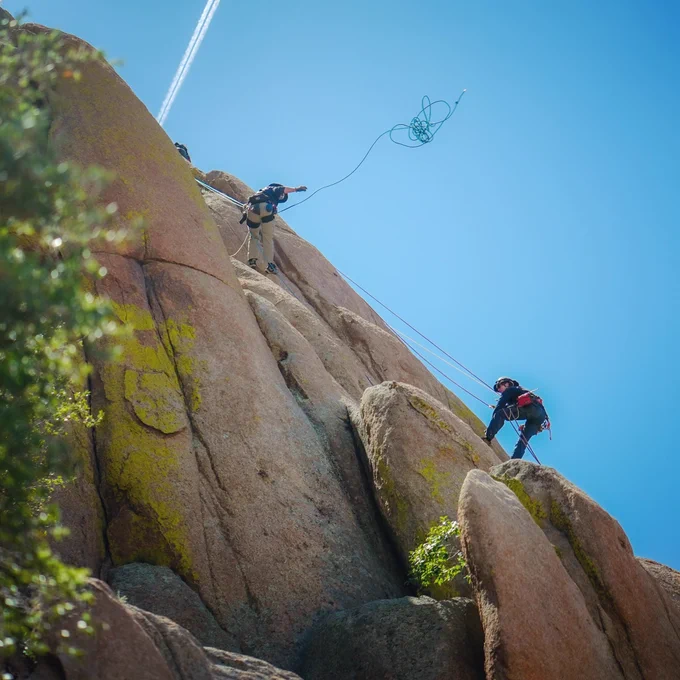 Firefighters train in technical rescue on the side of a mountain in Prescott, Arizona. One firefighter throws a rope to a second firefighter.