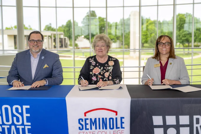 The Presidents of Rose State College, Seminole State College, and Redlands Community College are seated at a table from left to right signing an agreement.