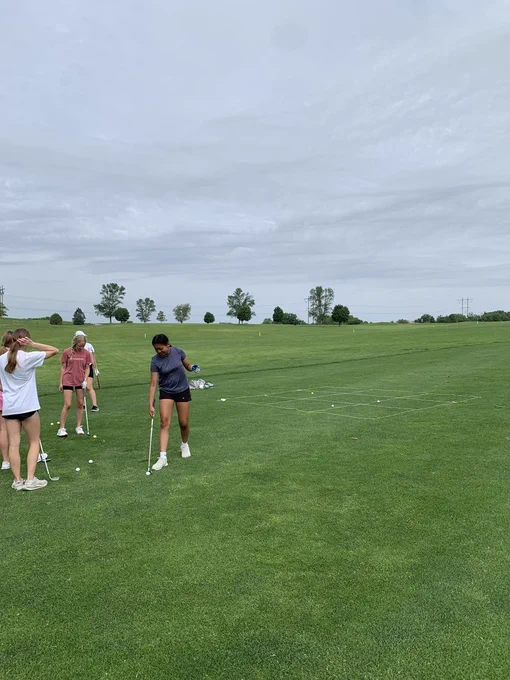 Four people on a golf course with one in focus, others blurry, under cloudy skies.