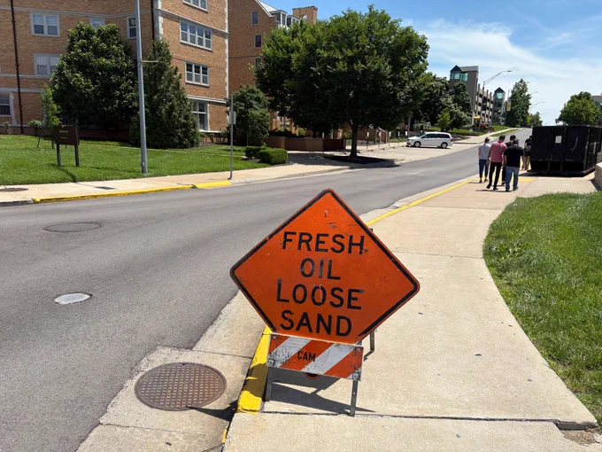 A sign that warns drivers to proceed with caution; fresh oil and loose sand may be ahead.