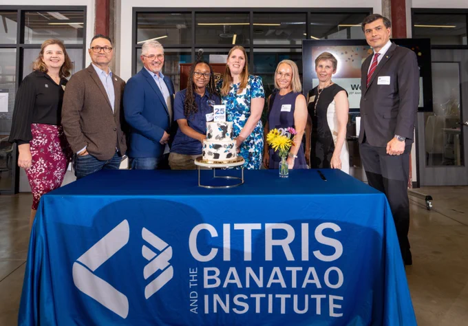 Group of eight people standing behind a table with a blue CITRIS and the Banatao Institute banner and a two-tier cake celebrating 25 years.