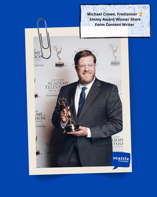 Michael Crowe in a gray suit holds his Emmy award. 