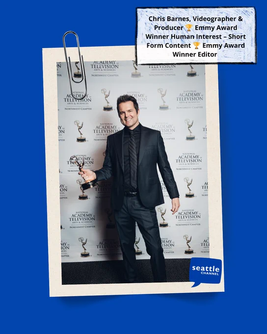 Chris Barnes in a black suit holds his Emmy award. 