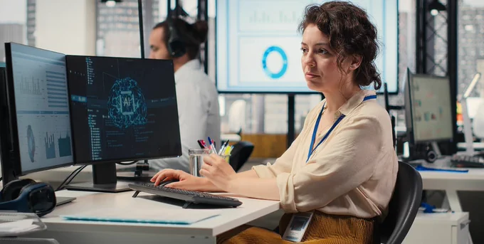 
Generate by AI Assist

An individual sits at a desk in a modern office environment, focusing on multiple computer screens displaying data and graphics. In the background, another person works at a separate desk. Large windows reveal a cityscape, and a presentation slide with charts is visible on a monitor.