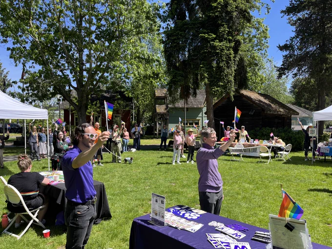 A group of people stand in a park waving various Pride flags. 