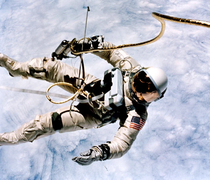 Backdropped by the clouds of Earth far below, astronaut Ed White wears a white spacesuit attached to the Gemini IV spacecraft (out of frame) by a gold umbilical. On June 3, 1965, he became the second human to perform an extravehicular activity, and the first American to do so. Credit: NASA/Jim McDivitt