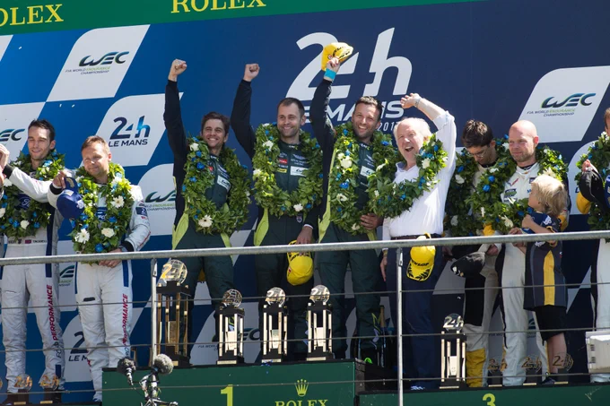 Aston Martin Racing drivers celebrating on Le Mans podium with trophies and laurel wreaths after class victory, FIA World Endurance Championship 24 Hours of Le Mans winners ceremony