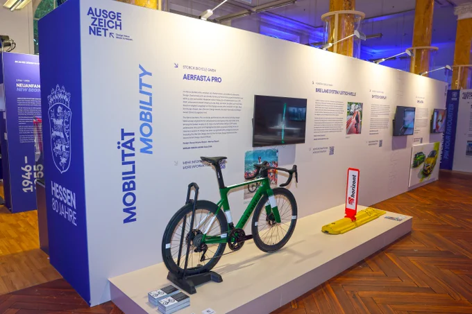 Ein Ausstellungsstand mit einem grünen Rennrad der Marke Aerfast.4 PRO und Informationen zu den Produkten des Herstellers Storch Bicycle GmbH.