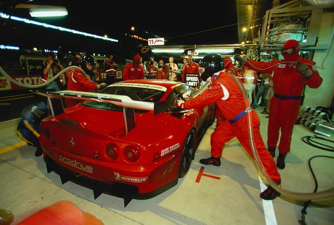 Night pit stop at 2002 24 Hours of Le Mans, Prodrive run Ferrari 550 GTS Maranello refuelled and serviced by crew in red overalls, mechanics working under pressure with fuel rig and tyre change during the endurance race.