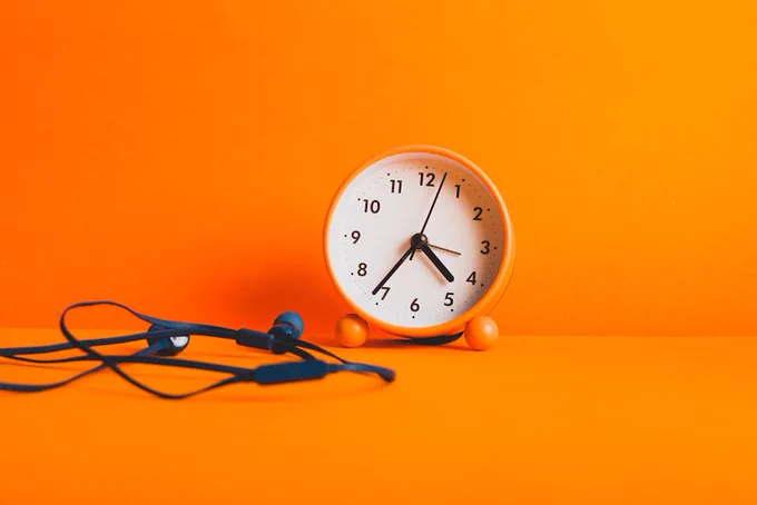 Vibrant orange clock and earphones on a matching orange surface, capturing minimalism and style.