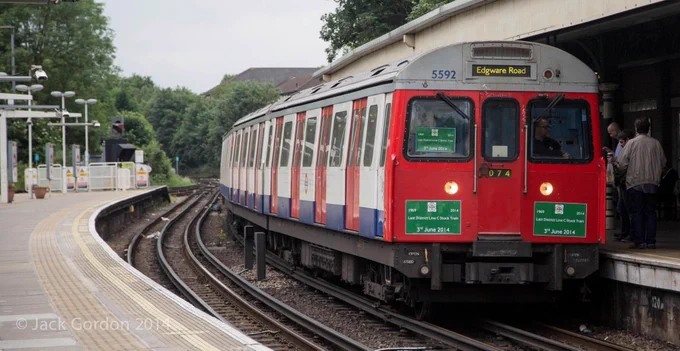 Viewed from the westbound platform, an eastbound C Stock train bound for Edgware Road calls at East Putney. The set number is 74 and three green notices have been stuck to the cab end and in the offside cab window: '1969 - 2014, Last District Line C Stock train, 3rd June 2014'