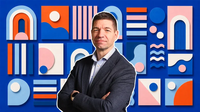Portrait of a person in a dark blazer with arms crossed, standing in front of a bold blue background filled with colorful geometric shapes, including arches, circles, lines, and abstract forms in orange, pink, white, and light blue