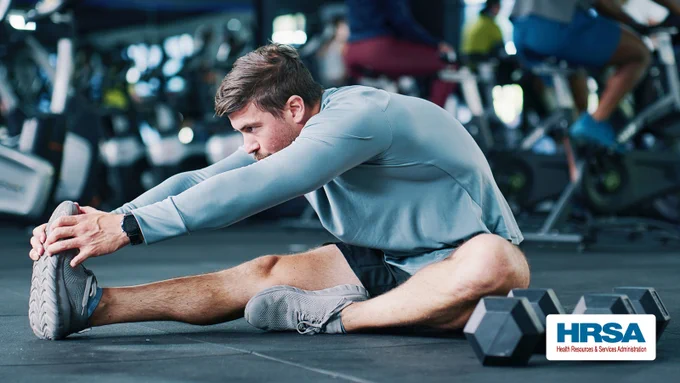 Man seated on the floor of a gym stretching
