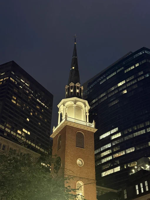 An old church tower illuminated against modern buildings at dusk. Boston.