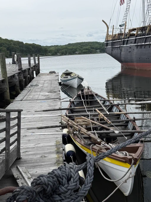 Dinghies next to a wooden dock, with an old whaling ship off to the right. Mystic, Connecticut.