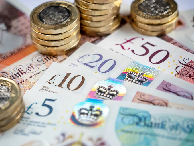 Close-up of British pound banknotes (£5, £10, £20, £50) with stacked one-pound coins on a flat surface.