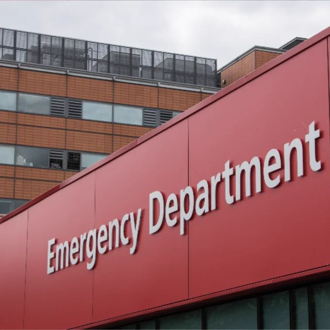 Red exterior wall with large white letters spelling Emergency Department on St Thomas' Hospital building under a cloudy sky.