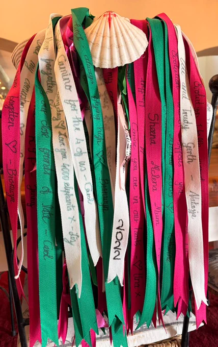 Red, green, and white ribbons with handwritten names and messages hanging over a chair, gathered beneath a scallop shell.