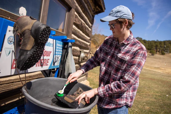 An angler scrubs mud and rocks from a boot at a gear cleaning station.