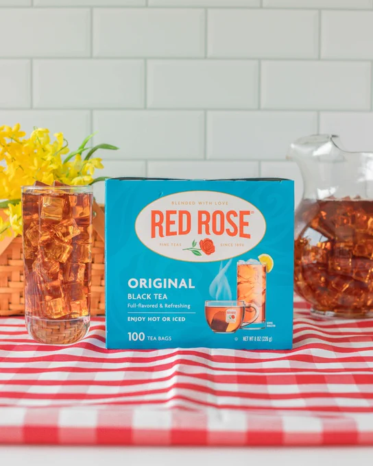 Box of Red Rose Original Black Tea with a glass of iced tea and a pitcher on a red and white checkered tablecloth.