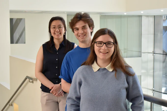 Jessie Xiao, Evan Ruesch and Emma Ibanez smile as they stand along a railing in MIT's Building 46.