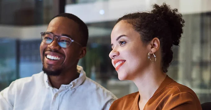 Two colleagues engaged in a focused discussion inside a modern office space with glass walls.