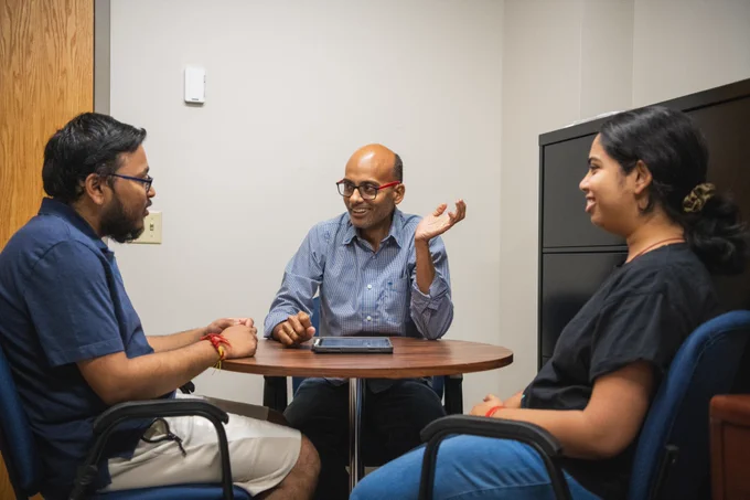 Bharath Sriperumbudur sitting at a table and speaking to two students.