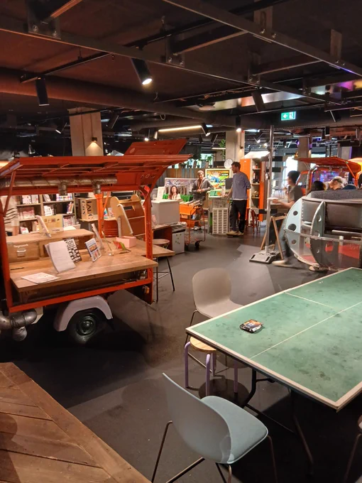 Indoor space with mobile book carts and people browsing in a modern, dimly lit bookstore or library.