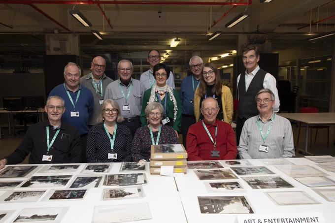 A group of people sat around a table covered in old photographs